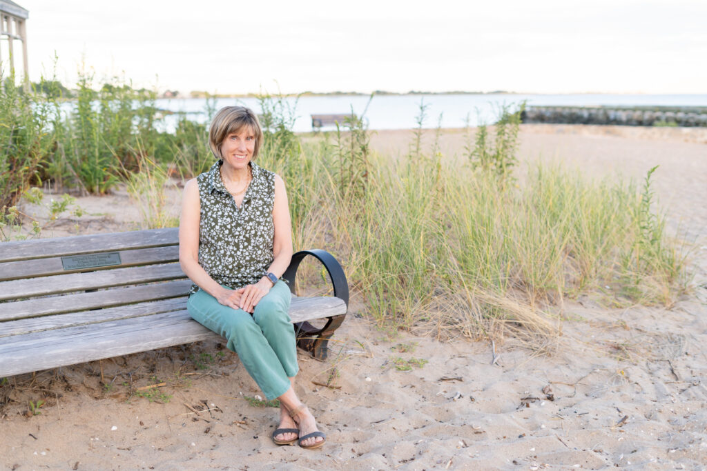 Photo of historical fiction author Kelly Scarborough sitting on a bench near East Wharf Beach in Madison CT
