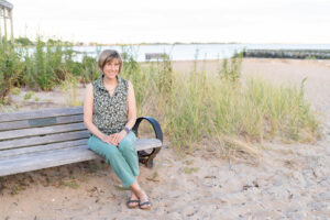 Photo of historical fiction author Kelly Scarborough sitting on a bench near East Wharf Beach in Madison CT