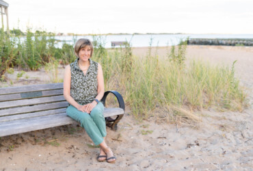Photo of historical fiction author Kelly Scarborough sitting on a bench near East Wharf Beach in Madison CT