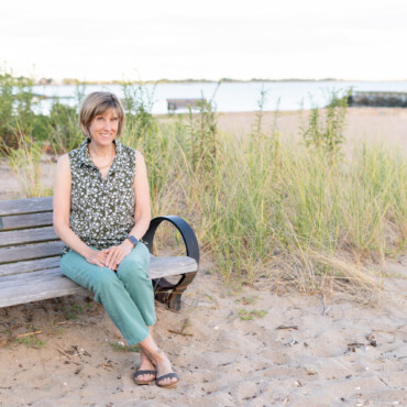Photo of historical fiction author Kelly Scarborough sitting on a bench near East Wharf Beach in Madison CT